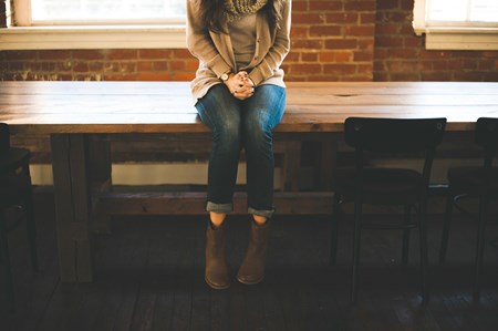 Frau sitzt ohne Selbstbewusstsein mit gefalteten Hände auf dem Tisch