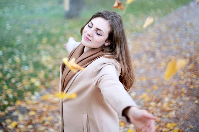 Eine Frau tanzt unter Herbstblättern, weil sie ein erfülltes Leben führt