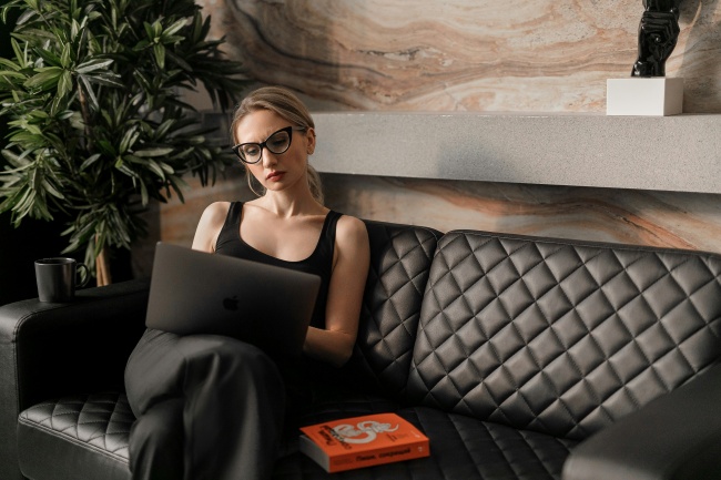 Eine Frau mit Brille und Laptop auf der Couch versucht perfektionistisch zu sein