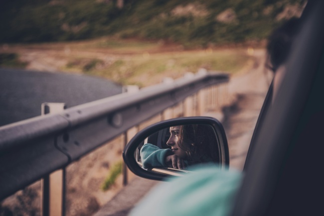 Eine Frau blickt aus dem Auto in den Rückspiegel - sie hat wie viele das Rückspiegelsyndrom