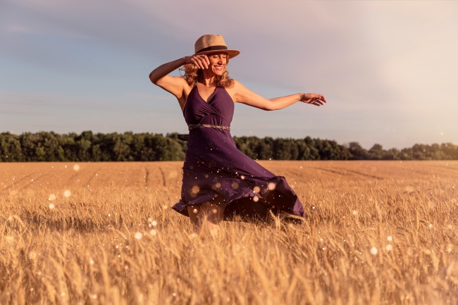 Eine Frau mit Hut im Weizenfeld freut sich - sie lässt ihr Rückspiegelsyndrom los