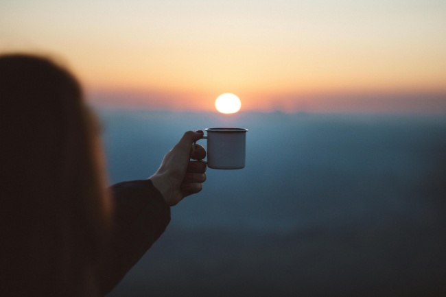 Eine Frau hebt eine Tasse Richtung Sonne und hört auf ihre Bauchgefühle
