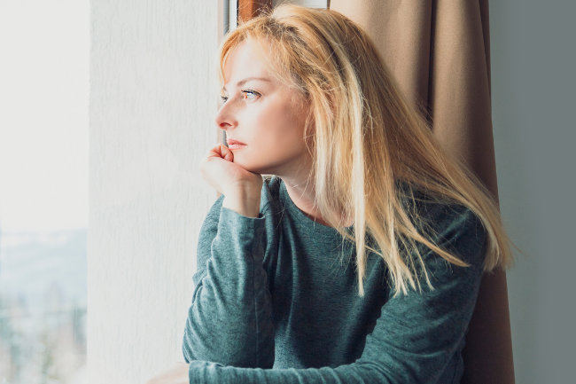 Nachdenkliche Frau sitzt am Fenster und blickt nach draußen – Symbol dafür, sich schnell angegriffen zu fühlen und Situationen persönlich zu nehmen.